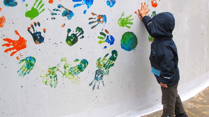 Ein Kind berührt eine Wand mit bunten Handabdrücken.