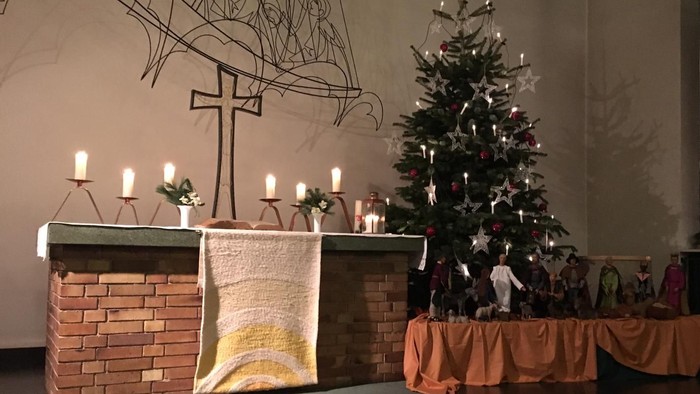 In der Kirche steht ein geschmückter Weihnachtsbaum neben einem Kamin mit Kerzen.
