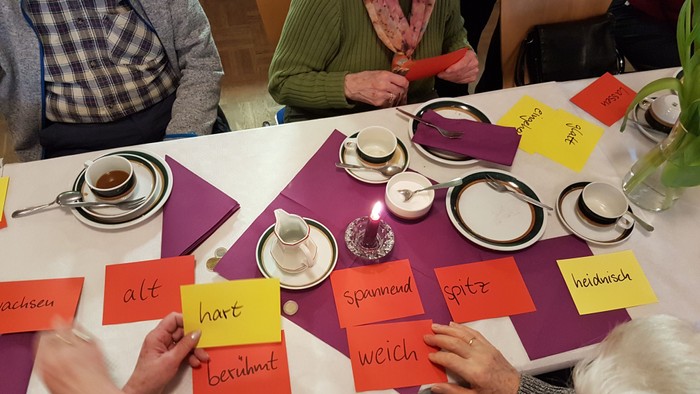 Senioren sitzen an einem Tisch und spielen ein Wortspiel mit Karten.