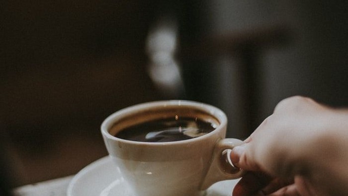 Eine Hand hält eine Tasse Kaffee auf einem Unterteller.
