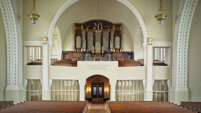 Große leere Kirche mit Holzpulten und Orgel im Hintergrund