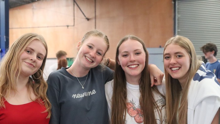 Four young women pose together, smiling, in a gymnasium.