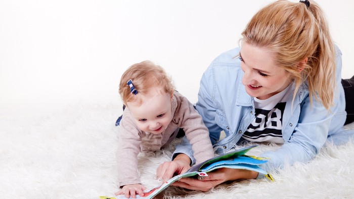 Eine Frau und ein Baby lesen gemeinsam ein Buch auf einem flauschigen Teppich.