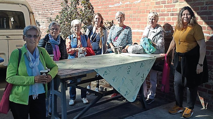 Eine Gruppe von Frauen steht um einen Picknicktisch, eine hält eine Tasse, eine andere ein Telefon.