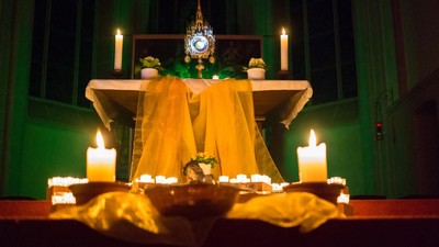 Kerzen beleuchteter Altar in einer Kirche mit gelbem Stoff und Monstranz.