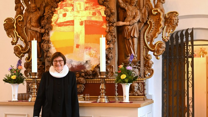 Kvinde i sort kåbe står foran et prægtigt religiøst alter med lys og blomster.