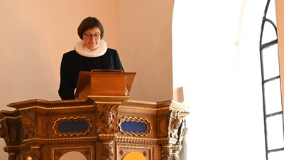 Kvinde på prædikestolen med åben bog, iført sort og hvidt tøj.