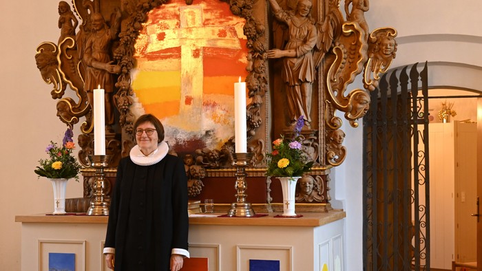 Kvinde i sort kjole, der står foran et religiøst alter med stearinlys og maleri.