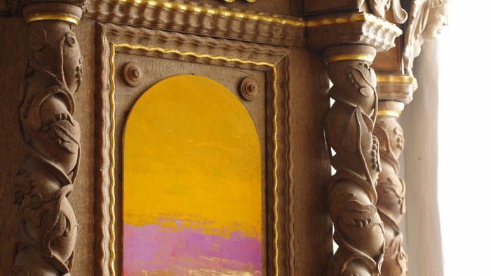 Udsmykket trævinduesramme, der fremviser en farverig solnedgangsscene med indviklede udskæringer og guld detaljer.