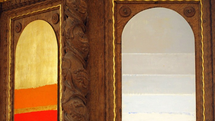 Udsmykket træbalkon med buede vinduer indrammet af indviklede udskæringer og gyldne detaljer.