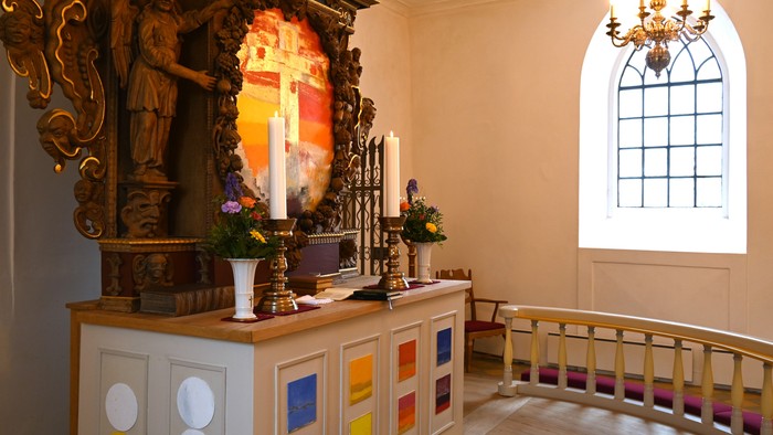 Elegant kapelalter med lys, religiøse statuer, farverige paneler og et roligt siddeområde.