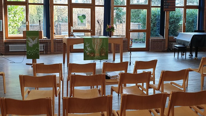 Ein Raum mit Holzboden, Stühlen und großen Fenstern, die auf einen Garten hinausgehen.