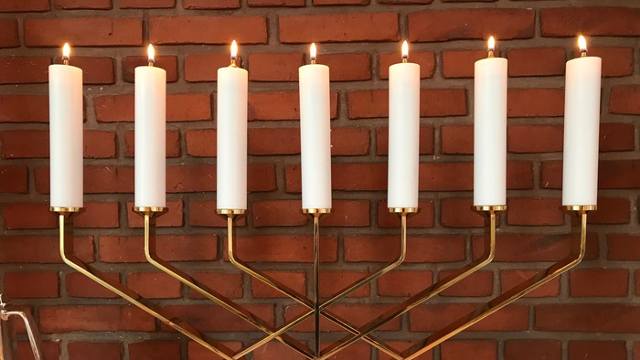 En gylden Menora med ni lysede lygter mod røde mursten.