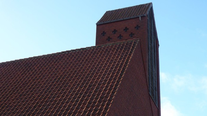 Røde teglmurstens kirke med spids tak og blå himmel