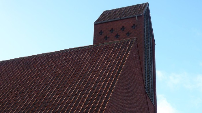 Røde teglmurstens kirke med spids tak og blå himmel