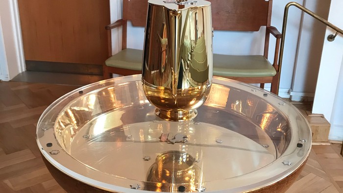 Elegant gylden kalk på en klar akrylstativ med træbase i et rum med træstole.