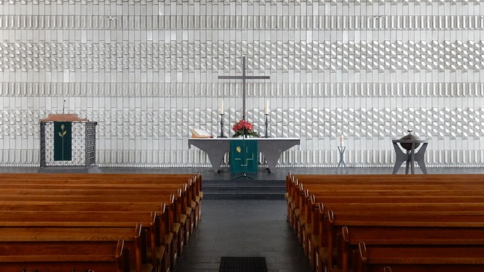 Leere Kirche mit Holzgestühl und Altarraum mit Kreuz und Kerzen