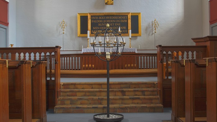 Kirkes interiør med alter, lysestage og træbænke.