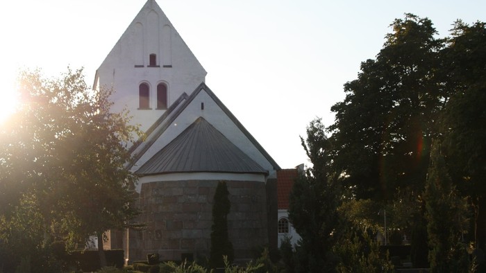 En hvid kirke med tårn og blå tag, omgivet af træer og buske.