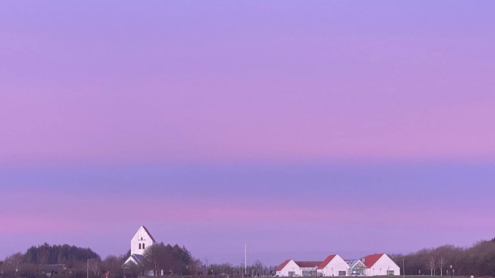 En rødlysende solgang over en åben landskab med en kirke og en gruppe svane.