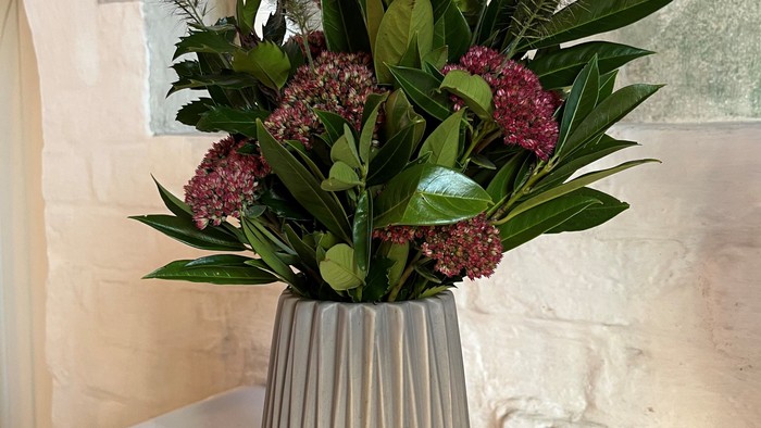 En blomsterstang i en sølvfarvet vase på bord.