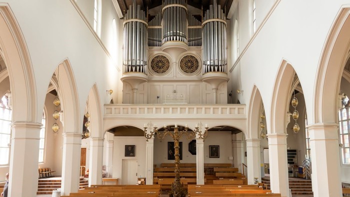 Innenansicht einer Kirche mit Orgel, hölzernen Bänken und hohen Rundbögen.