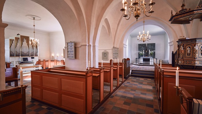 Indre del af kirke med bænke, orgel og lysstake