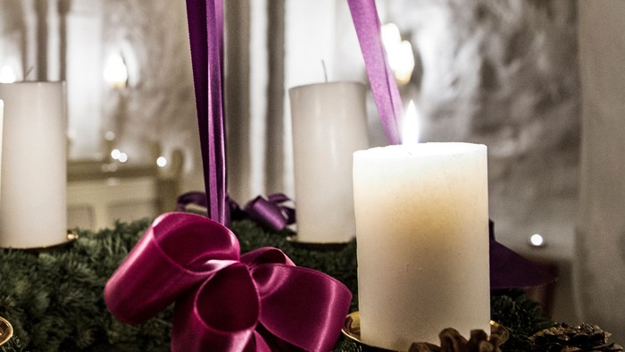 En adventskranse med tre lysende lygter og grønne nåletræer med røde bælter.