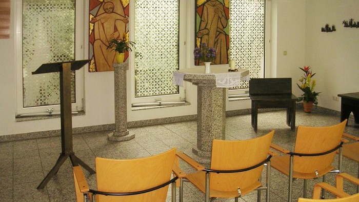 Modernes Kircheninnere mit bunten Fenstern und gelben Stühlen