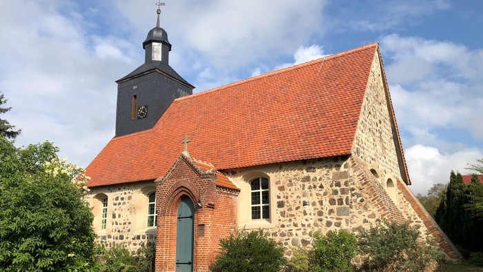 Kleine Kirche mit rotem Dach und Turm, umgeben von Grün.