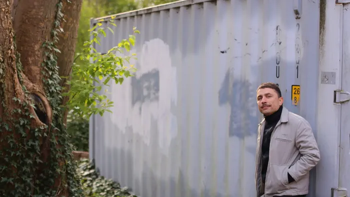 En mand står ved en hvid container med graffiti på en mur.