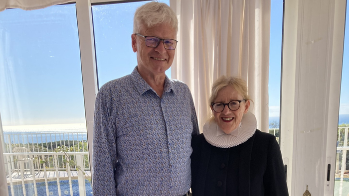 En ældre mand og kvinde står sammen i et rum med udsigt til havet