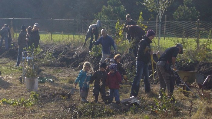 Eine Gruppe von Menschen arbeitet in einem Garten, Kinder helfen mit.