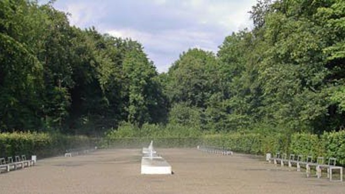 Ein großer Park mit einem weißen Brunnen und umgeben von Bäumen und Büschen