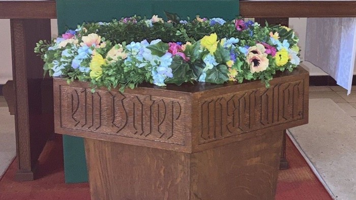 Das Foto zeigt das Holzverkleidete Taufbecken mit einem Kranz aus Blüten.