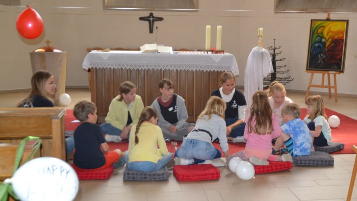 Kinder in bunten Kostümen sitzen in den Kirchenbänken einer Kirche.