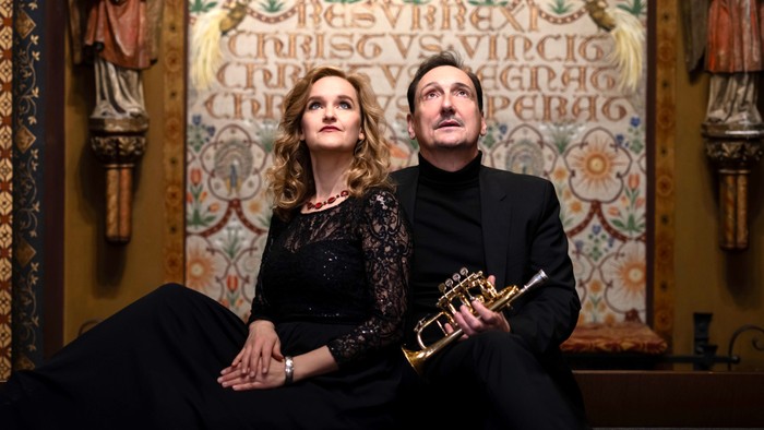 Elegantes Paar posiert mit einer Trompete vor einem verzierten, klassischen Hintergrund.