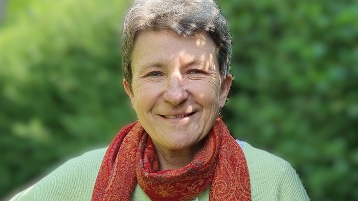 Person, der smiler, iført en grøn jakke og et rødt mønstret tørklæde udendørs.