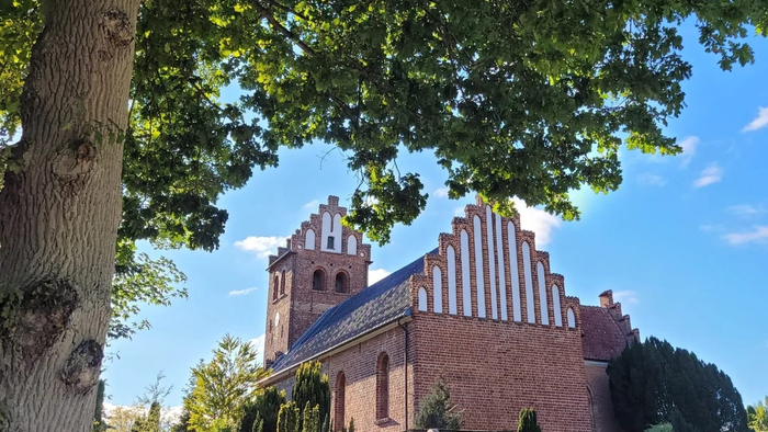 Et rødt teglkirke med spisse tårne og blå tag, omgivet af træer og en mur.