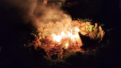 Ein Lagerfeuer brennt hell, während Holzscheite und Glut in der Nacht leuchten.