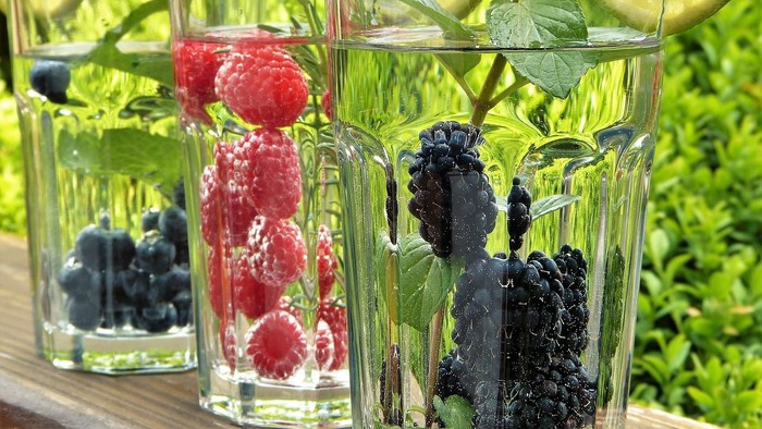 Drei Gläser mit Wasser, Früchten und Zitronenscheiben auf Holztisch