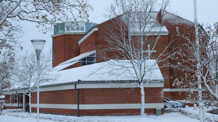 En rød murstensbygning med sne på taget og træer.