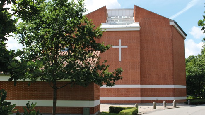 Et rødt murstenskirke med kors på fasaden og træ foran