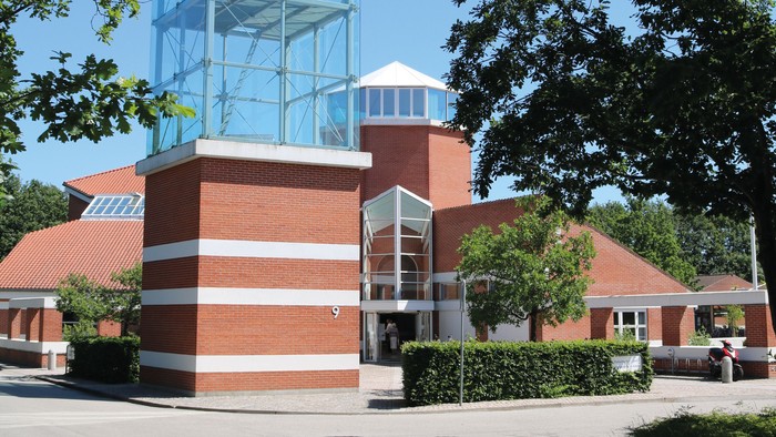 Et moderne glasbygning i en parkagtig omgivelse