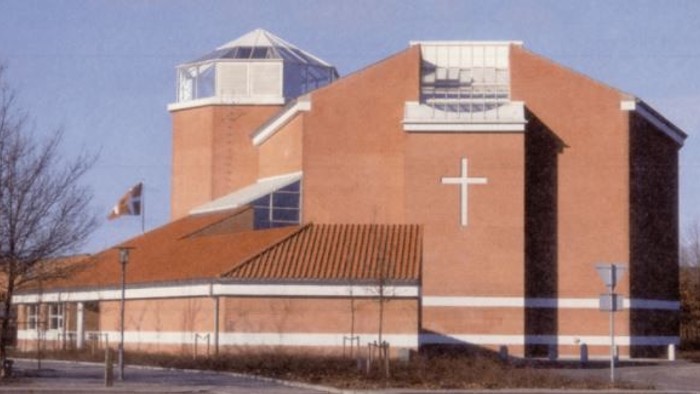 En rød kirke med et stort kors på fasaden og en klokketårn.