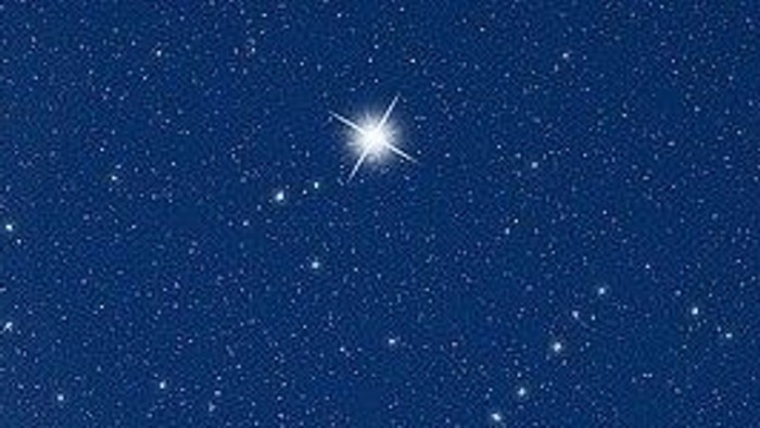 En klar stjerne skinner tydeligt på en klar nattehimmel fyldt med utallige mindre stjerner.