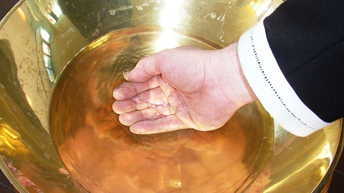 En hånd rynker i en guldfarvet vase på en træstol