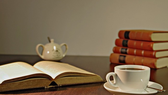 Ein offener Buch, eine Teekanne und eine Tasse Tee auf einem Holztisch