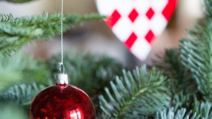 En rød glaskugle hænger på en julgran sammen med et hjerteformet pynt.