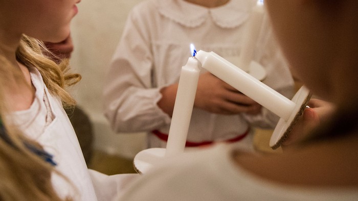To børn i hvide klæder lader lys på candlesticks